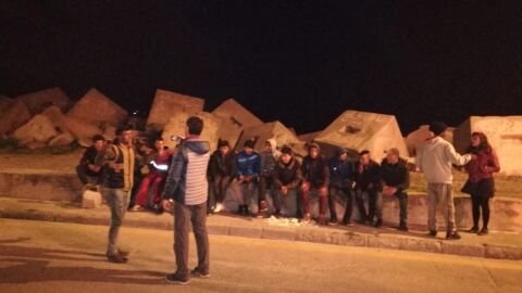 Bel&eacute;n Delgado junto a los menores no acompa&ntilde;ados en el puerto de Ceuta, durante el reparto de bocadillos. Los j&oacute;venes duermen entre las escolleras que se ven al fondo