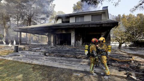 Dos bomberos ante una de las viviendas afectadas por el incendio forestal de Llutxent 