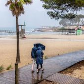 Dos personas se protegen de la lluvia, mientras pasean por la playa de Camp de Mar, en Mallorca.