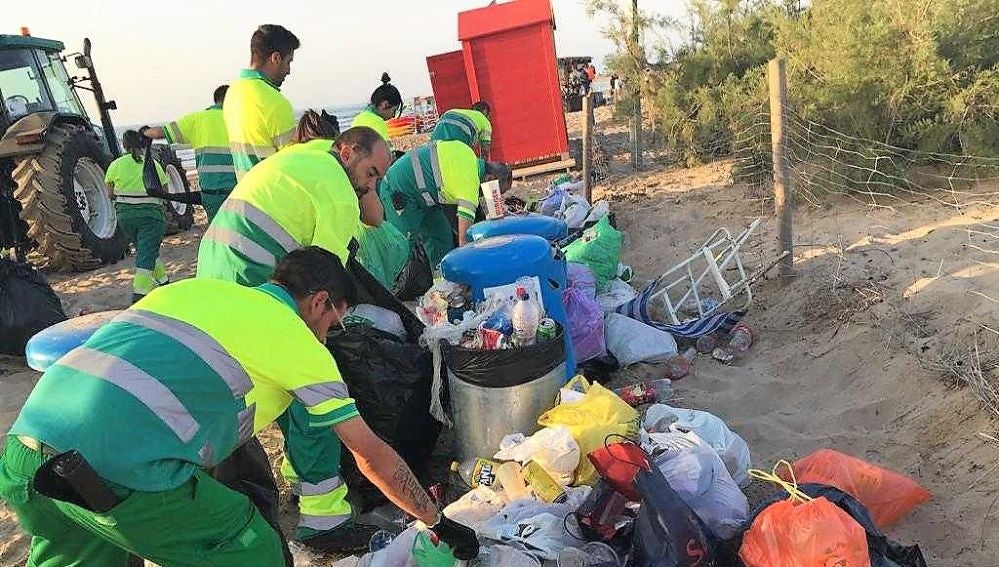 Trabajadores de Urbaser recogen basura en una playa de Elche tras la noche de San Juan de 2019. 