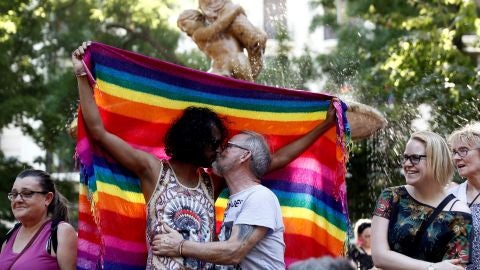 Dos hombres bes&aacute;ndose ante la bandera del orgullo gay