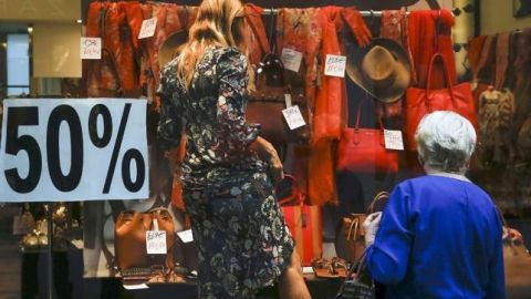 na mujer observa cómo una dependienta etiqueta los artículos del escaparate durante las rebajas_643x397