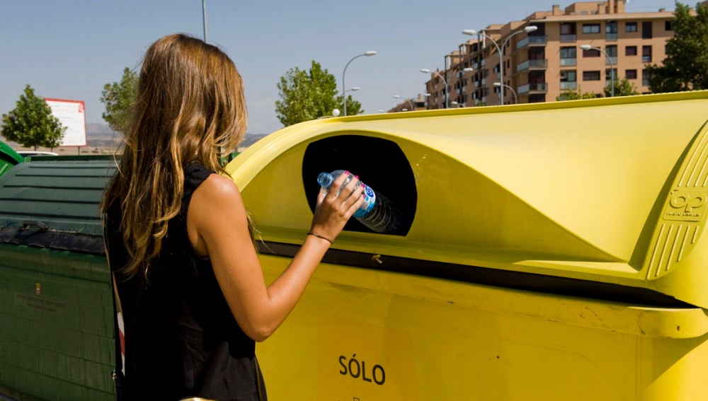 Una mujer deposita una botella de plástico en un contenedor amarillo.