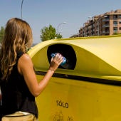 Una mujer deposita una botella de plástico en un contenedor amarillo.