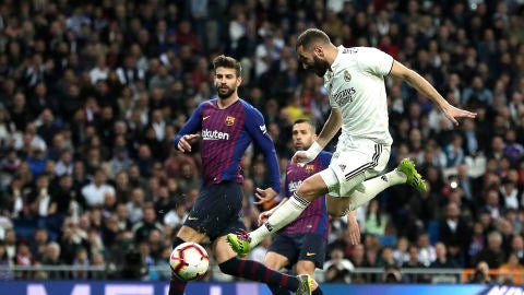 Benzema dispara a puerta ante la defensa de Piqu&eacute; durante un Cl&aacute;sico