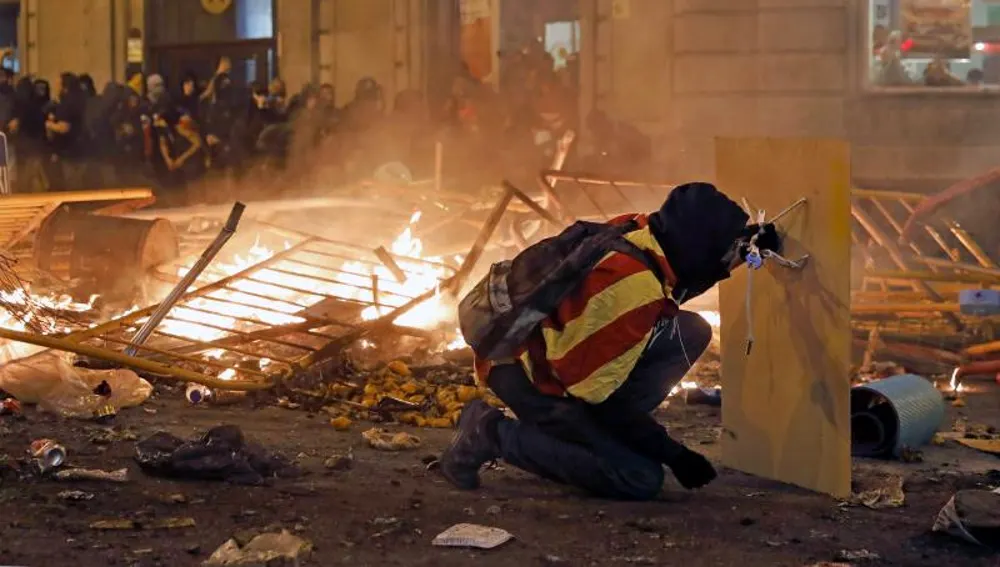 Un manifestante se protege con una plancha de madera durante los disturbios en Barcelona