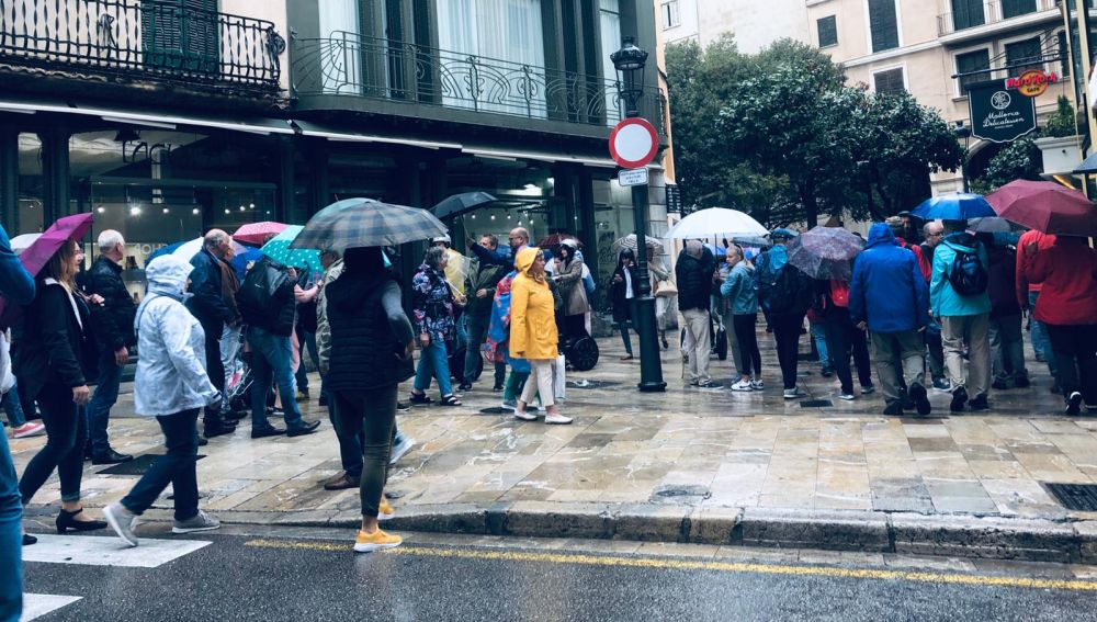 Ciudadanos paseando bajo la lluvia en el centro de Palma.