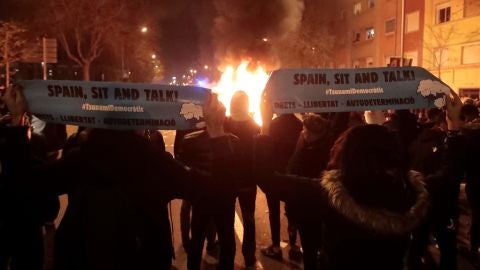 Manifestantes de Tsunami Democr&agrave;tic frente a un contenedor quemado