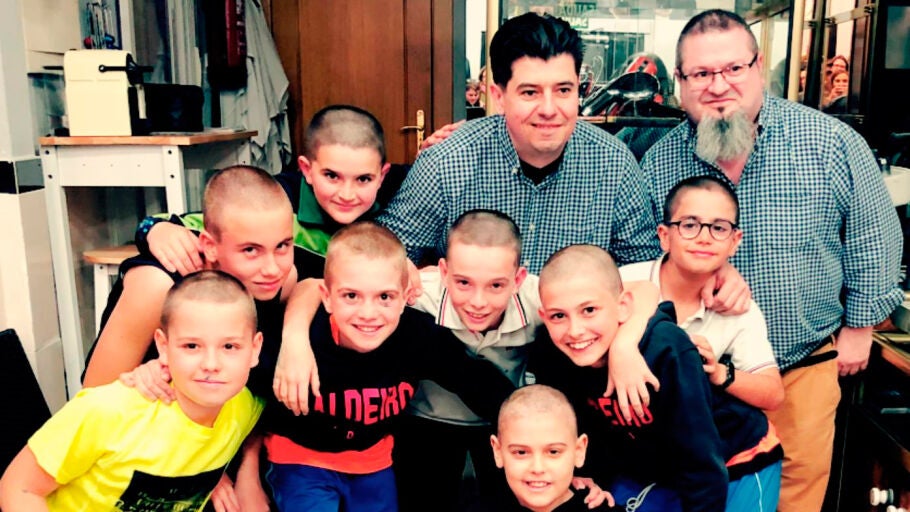Los ni&ntilde;os ya rapados junto a su amigo posan junto a los peluqueros