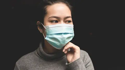 Una mujer con mascarilla tocándose la cara Una mujer con mascarilla tocándose la cara