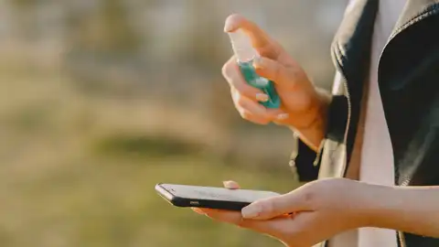 Una mujer desinfectando su teléfono móvil Una mujer desinfectando su teléfono móvil