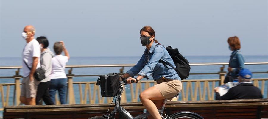 Una mujer pasea en bicicleta protegida con una mascarilla Una mujer pasea en bicicleta protegida con una mascarilla