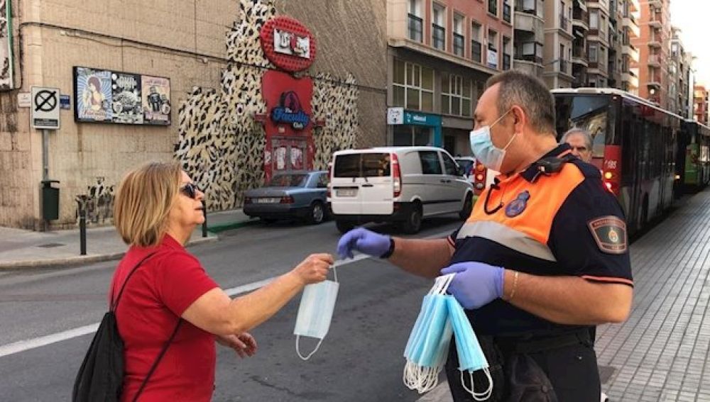 Un voluntario de Protección Civil entrega una mascarilla a una mujer en Elche.