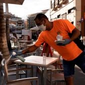 Un camarero desinfecta unas sillas de una terraza de un bar.