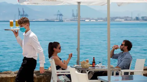 Un camarero con mascarilla pasa ante una pareja que almuerza en un restaurante de Málaga Un camarero con mascarilla pasa ante una pareja que almuerza en un restaurante de Málaga
