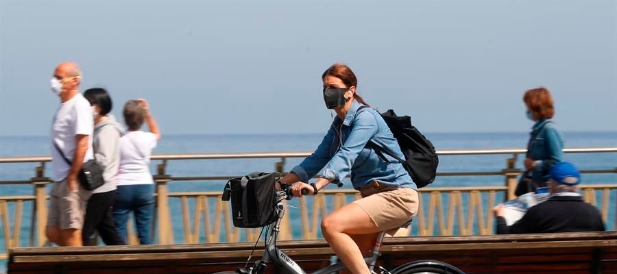 Una mujer pasea en bicicleta protegida con una mascarilla por el paseo de la Zurriola de San Sebastián Una mujer pasea en bicicleta protegida con una mascarilla por el paseo de la Zurriola de San Sebastián
