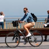 Una mujer pasea en bicicleta protegida con una mascarilla por el paseo de la Zurriola de San Sebastián