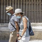 Dos personas caminan con mascarilla y sombrero