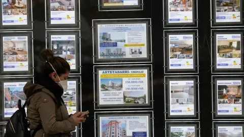 Una mujer pasa por delante de un portal inmobiliario de venta y alquiler Una mujer pasa por delante de un portal inmobiliario de venta y alquiler