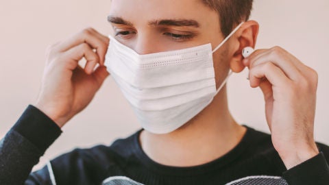 Un joven con mascarilla usa auriculares