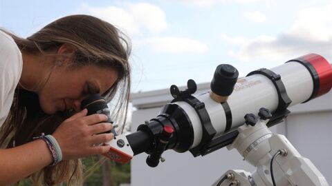 Una chica observa a trav&eacute;s de un telescopio.