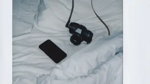 Una cámara de fotos y un móvil en una cama Una cámara de fotos y un móvil en una cama
