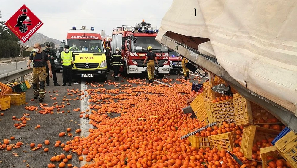 Servicios de emergencias junto al camión y la carga de naranja.