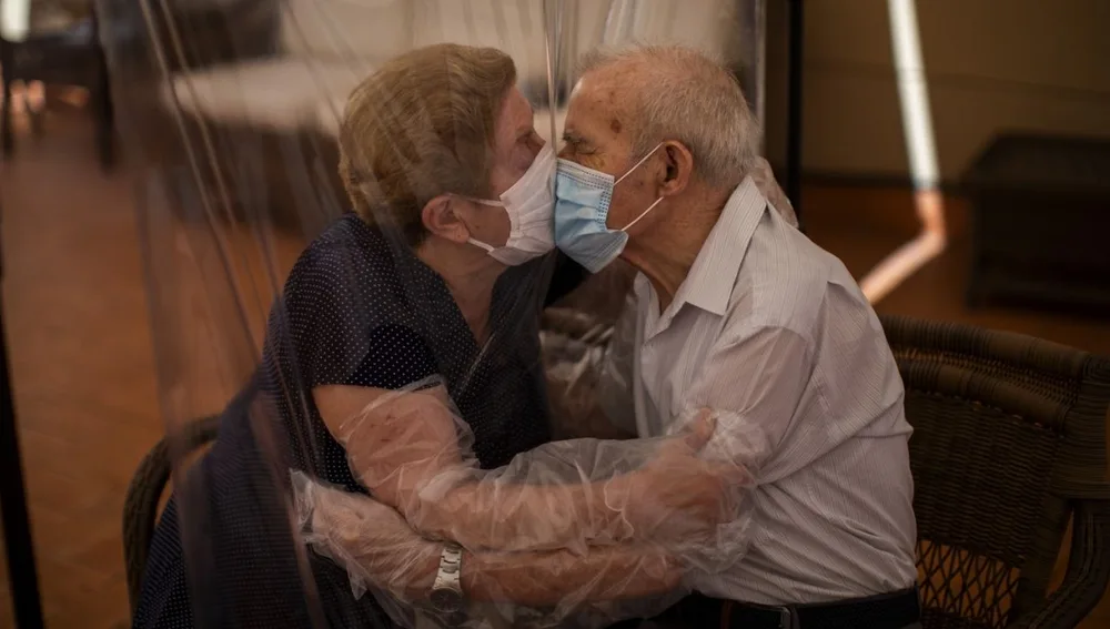 Una pareja de ancianos se besa con un plástico entre medias para evitar contagiarse.