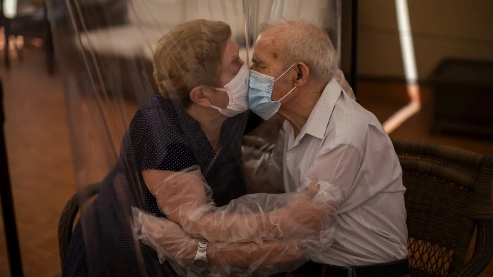 Una pareja de ancianos se besa con un plástico entre medias para evitar contagiarse.