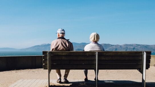 Dos ancianos sentados en un banco mirando hacia el horizonte costero