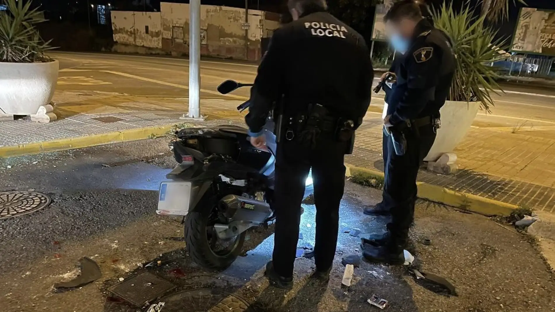 Dos agentes de la Policía Local de Elche junto a la moto dañada por el detenido.