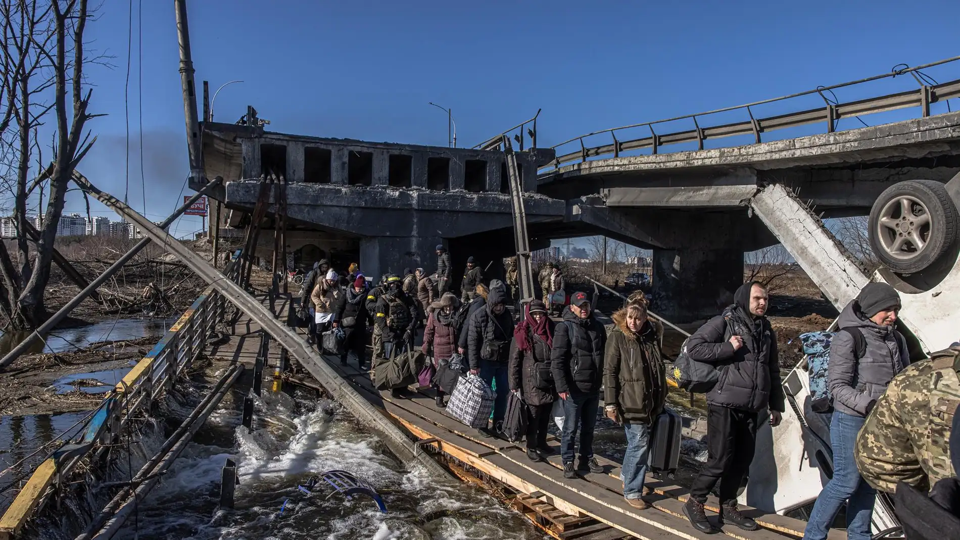  Civiles ucranianos cruzan con su equipaje un puente destruido mientras huyen de Irpin, una región de Kiev.