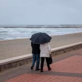 Dos personas pasean por la playa bajo la lluvia