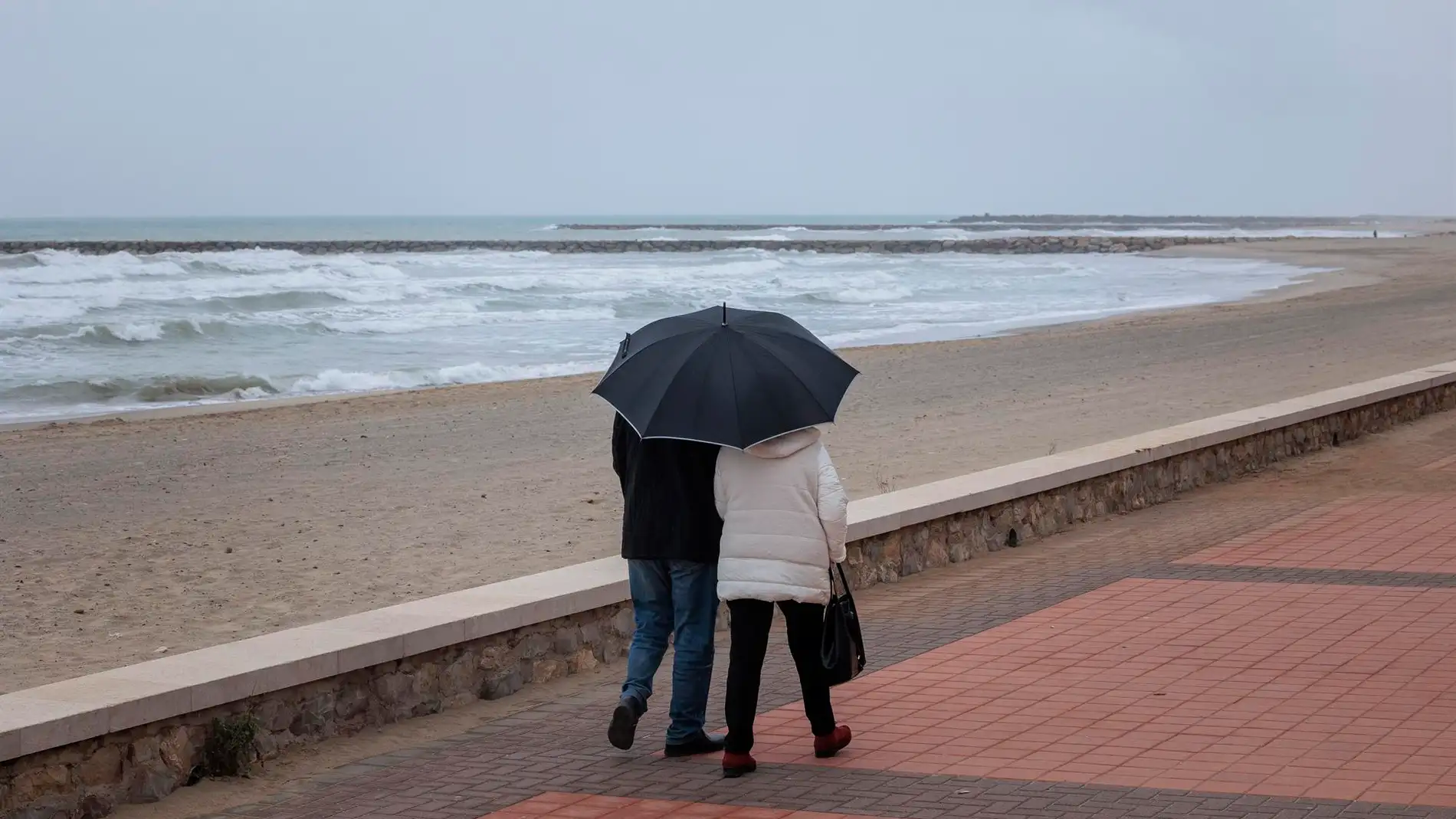 Dos personas pasean por la playa bajo la lluvia