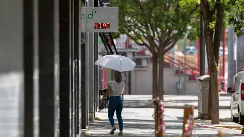 Una mujer camina por una calle bajo un termómetro que indica los 47ºC