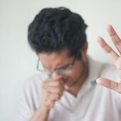 Imagen de archivo de un hombre tosiendo con la mano levantada