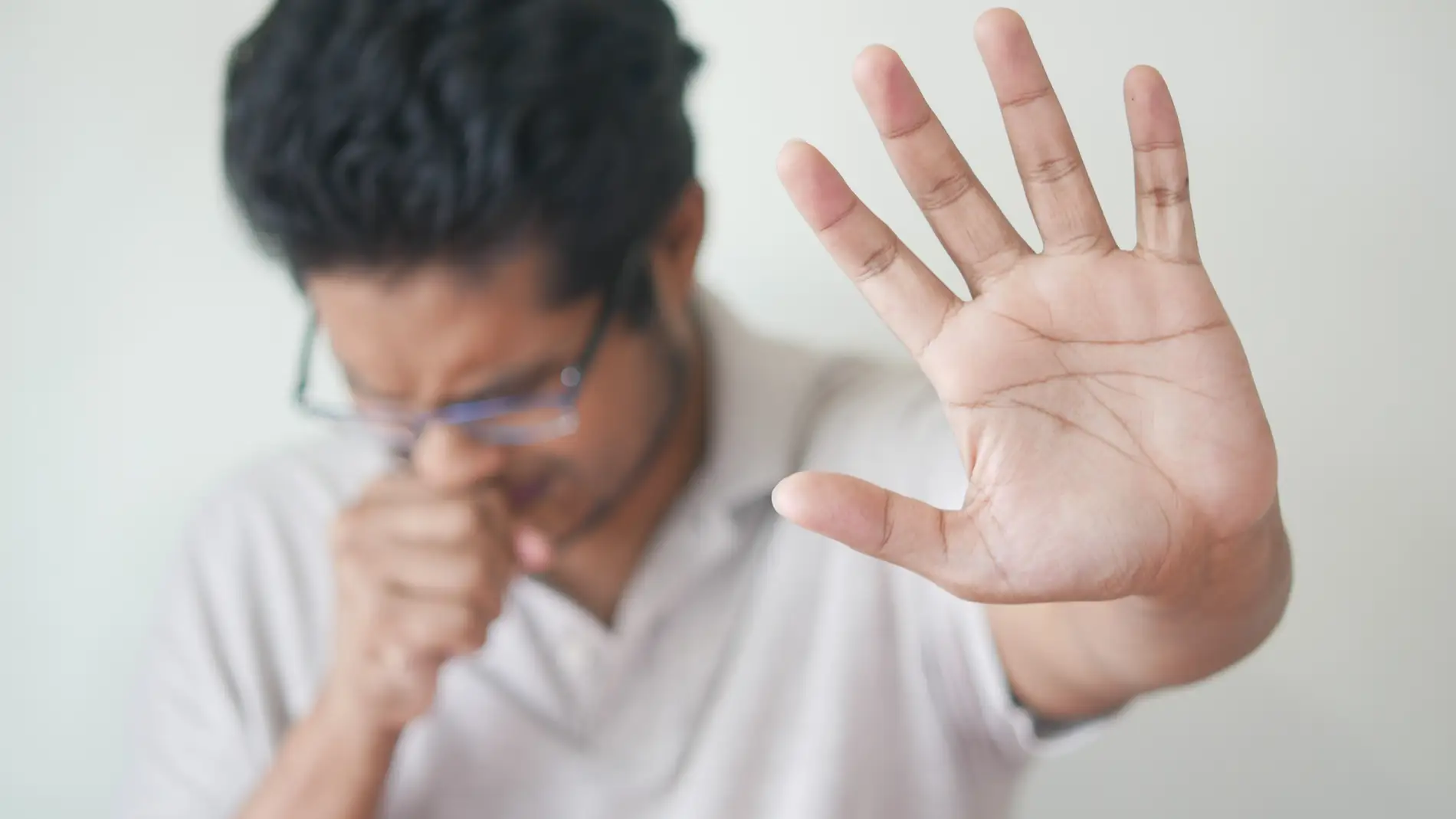 Imagen de archivo de un hombre tosiendo con la mano levantada/ Unsplash