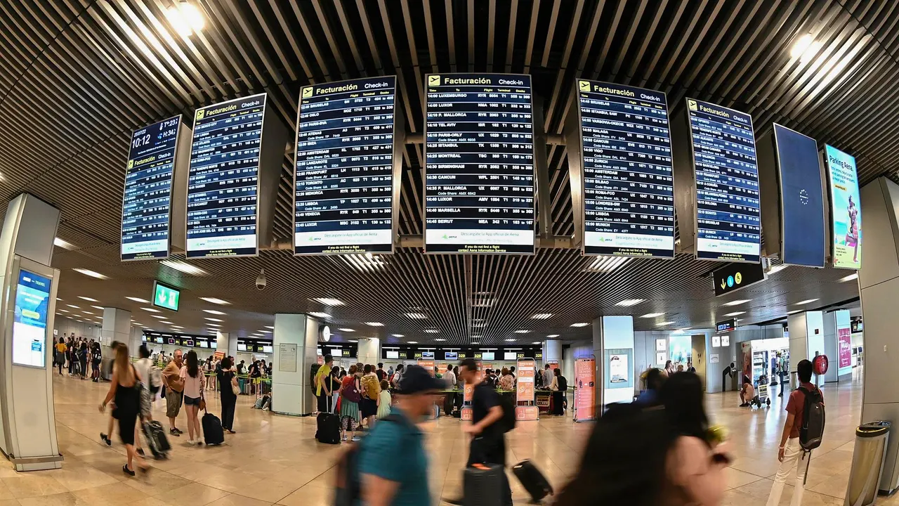 Varios pasajeros pasan por las pantallas de información en el aeropuerto Adolfo Suárez Madrid-Barajas.