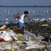 Un niño salta entre las basuras llevadas por el mar a la costa de Manila