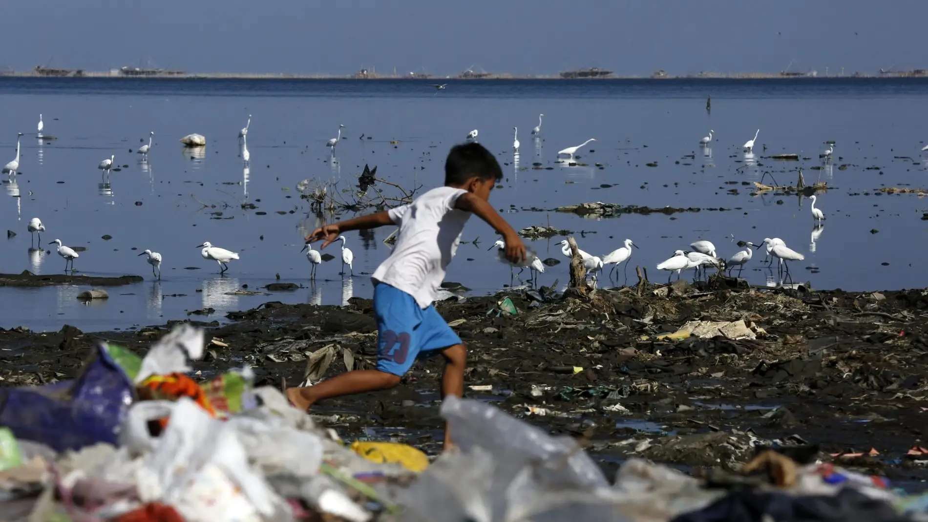 Un niño salta entre las basuras llevadas por el mar a la costa de Manila