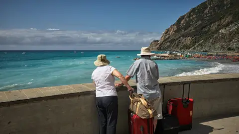 Imagen de archivo de dos personas mayores, de espaldas, mirando al mar junto a un par de maletas rojas