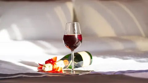 Copa de vino y botella de champagne en una cama Copa de vino y botella de champagne en una cama