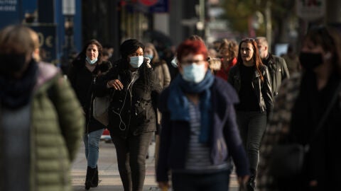 Varias personas pasean por la calle con mascarilla.