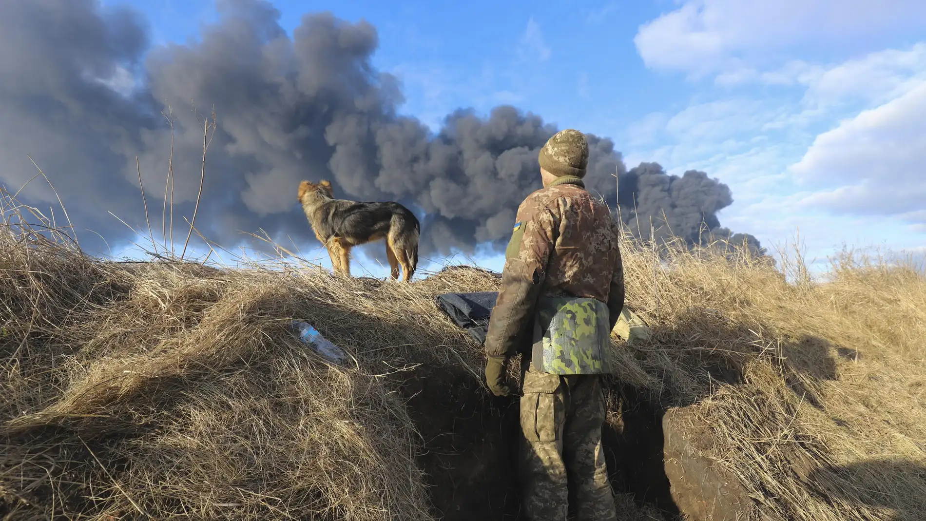 Un militar ucraniano observa junto a su perro una columna de humo negro cerca de Kiev