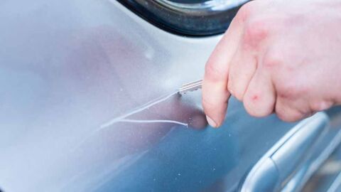 Un hombre rayando un coche con una llave