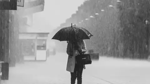 Imagen de archivo de una mujer paseando bajo la lluvia La AEMET desvela qué días lloverá en Semana Santa