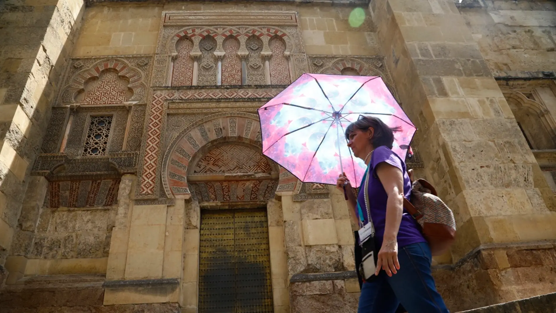 Una mujer se resguarda del sol con una sombrilla mientras camina junto a la Mezquita-Catedral de Córdoba/ EFE/Salas