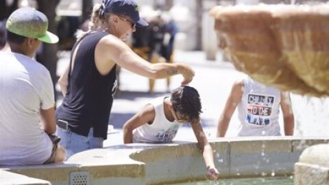 Una madre refresca a su hijo echándole agua de una fuente por la cabeza