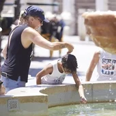 Una madre refresca a su hijo echándole agua de una fuente por la cabeza Una madre refresca a su hijo echándole agua de una fuente por la cabeza