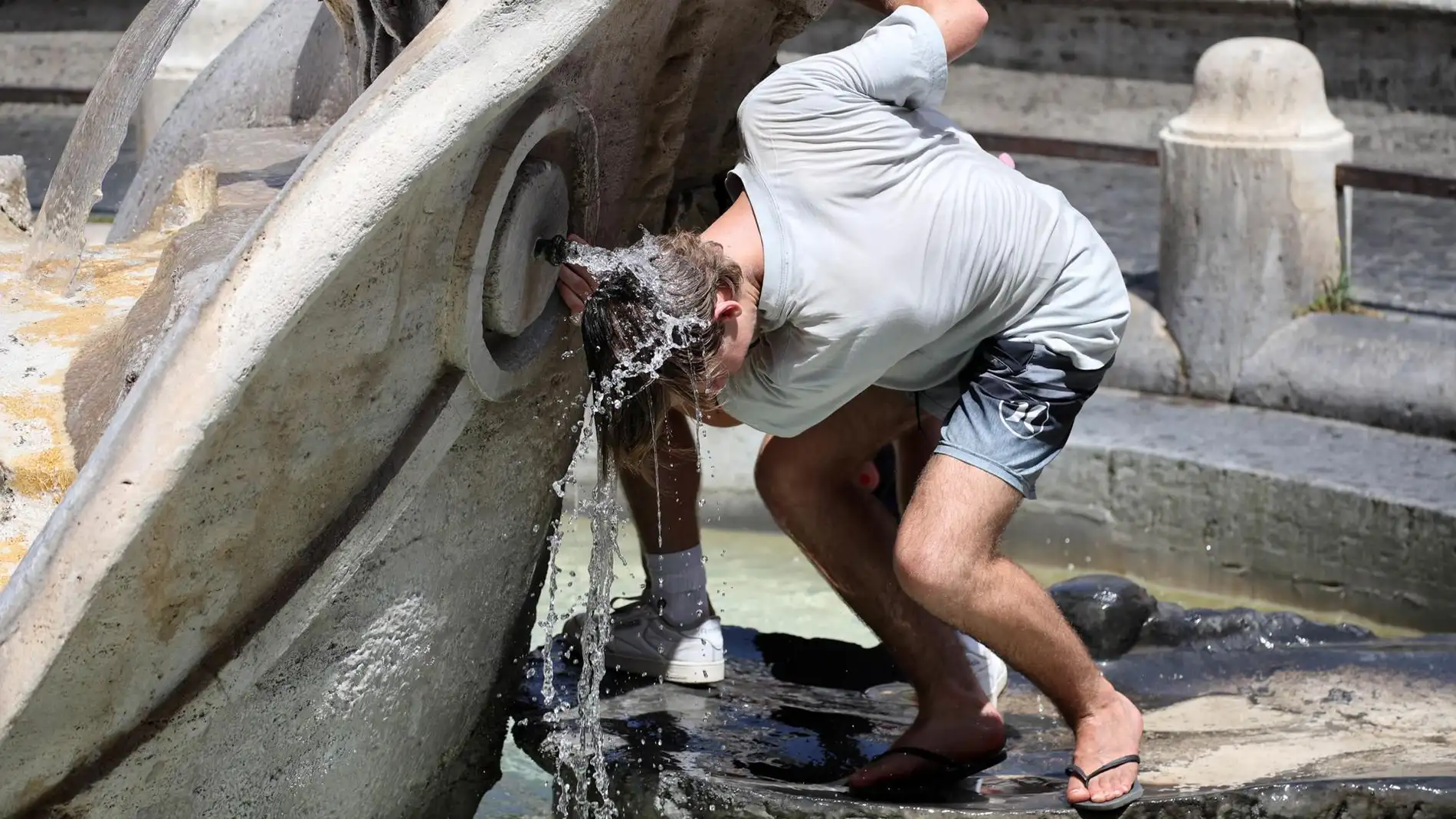 Un hombre se refresca bajo una fuente en Roma